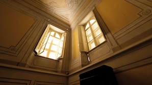 Quarto com detalhes ornamentais no teto e duas janelas com portadas.