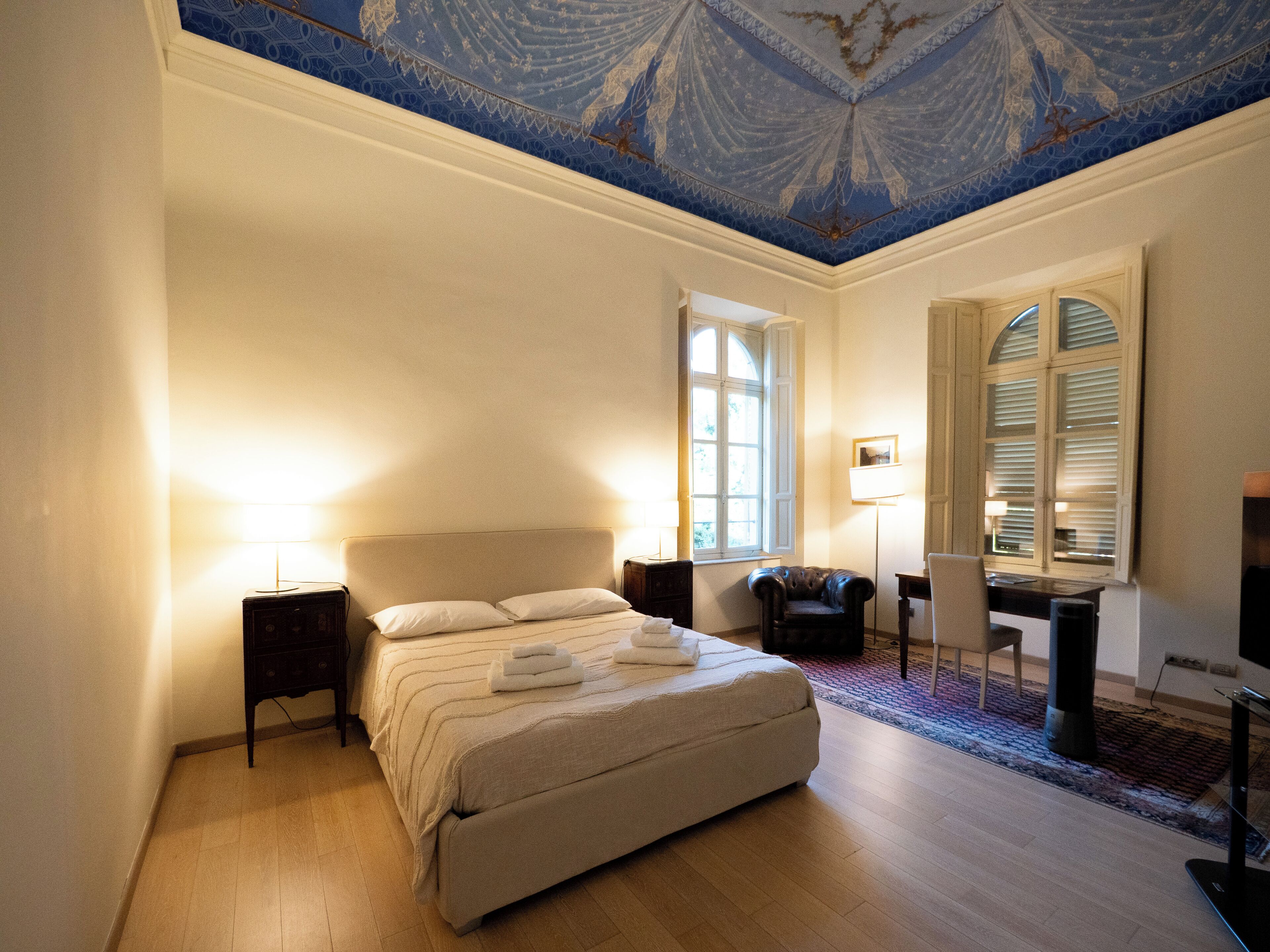 A bedroom with a large bed, a desk, a chair, and a television.