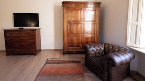 Um quarto com um armário de madeira, uma poltrona de couro, uma televisão sobre uma cômoda de madeira e um tapete estampado.