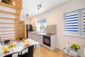 A modern kitchen with a dining area, wooden ladder, and a view of the outdoors through the window. - Seaside Escape Mielenko | Baltic Coast Cottages by North Apartments (Mielenko)