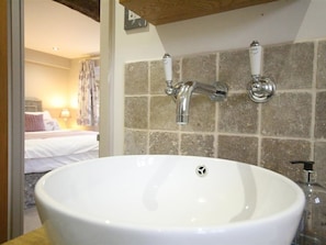 A bathroom with a large white sink, two wall-mounted faucets, and a stone-tiled wall. - The Coach House (Burford)