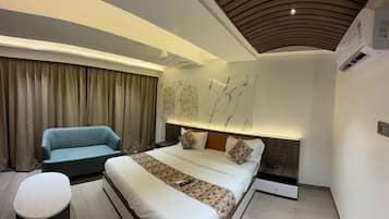 A modern bedroom with a large bed, a sofa, a bedside table, and a wall-mounted light fixture.