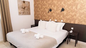 Un lit bien fait, avec une couette blanche et des oreillers, une table de chevet avec un téléphone, et un mur orné d’un motif géométrique.