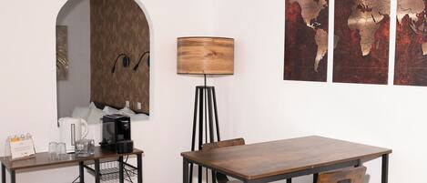 Un coin repas compact avec une table et des chaises en bois, un petit réfrigérateur, une lampe et une œuvre d’art représentant une carte du monde accrochée au mur.