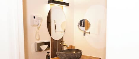 A bathroom with a wooden vanity, a large mirror, a toilet, and a towel dispenser.