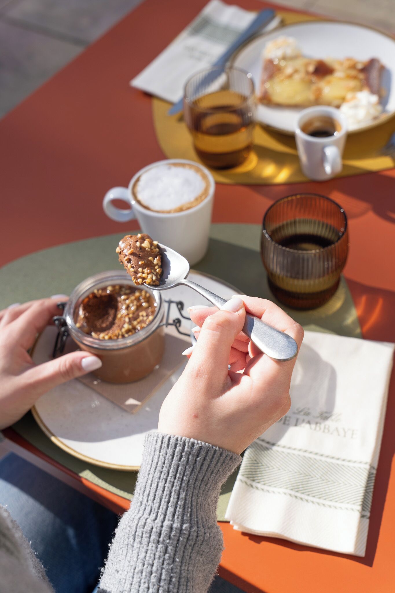 Una persona comiendo un postre con cuchara, una taza de café y un vaso de agua sobre una mesa.