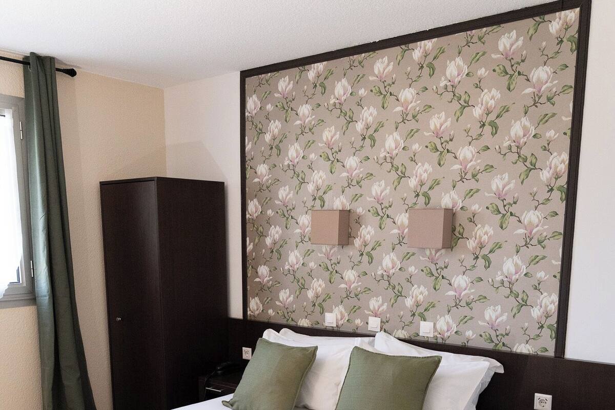 Un lit bien fait, avec des oreillers, un plaid vert et des serviettes enroulées.