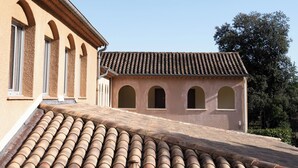 Un bâtiment doté d’un toit en tuiles, de fenêtres en arc de cercle et d’une terrasse sur le toit à surface plane.