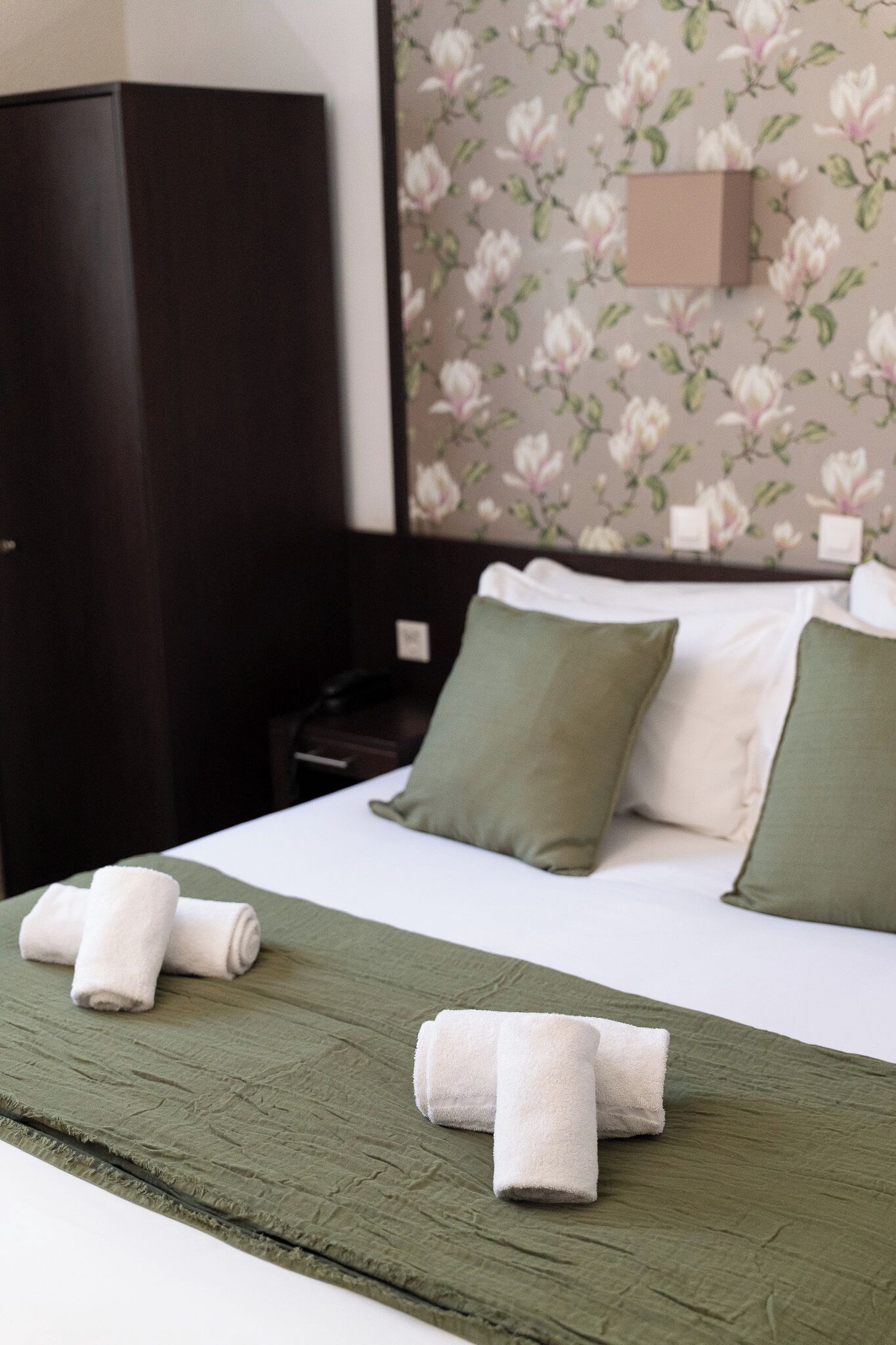 Una cama bien hecha con almohadas verdes y blancas, una colcha verde y dos toallas enrolladas sobre la cama.