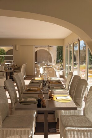 Een eetgedeelte met een lange tafel voor zes personen, omringd door rieten stoelen, met uitzicht op de omgeving door grote ramen.