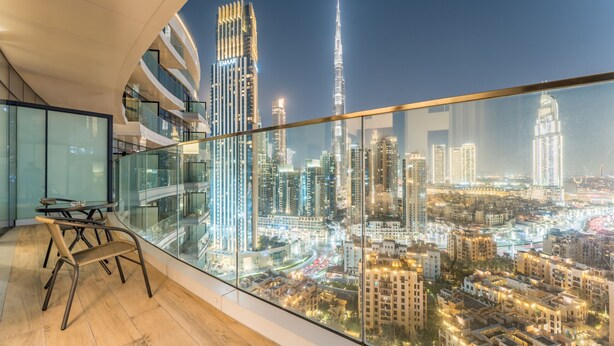 Un interior moderno con un balcón de vidrio que ofrece vistas a un paisaje urbano nocturno, con rascacielos iluminados y una vista del área urbana.
