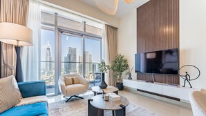 Una sala moderna con un televisor grande, un sofá azul, un sillón color beige y vistas de la silueta urbana a través de ventanales.