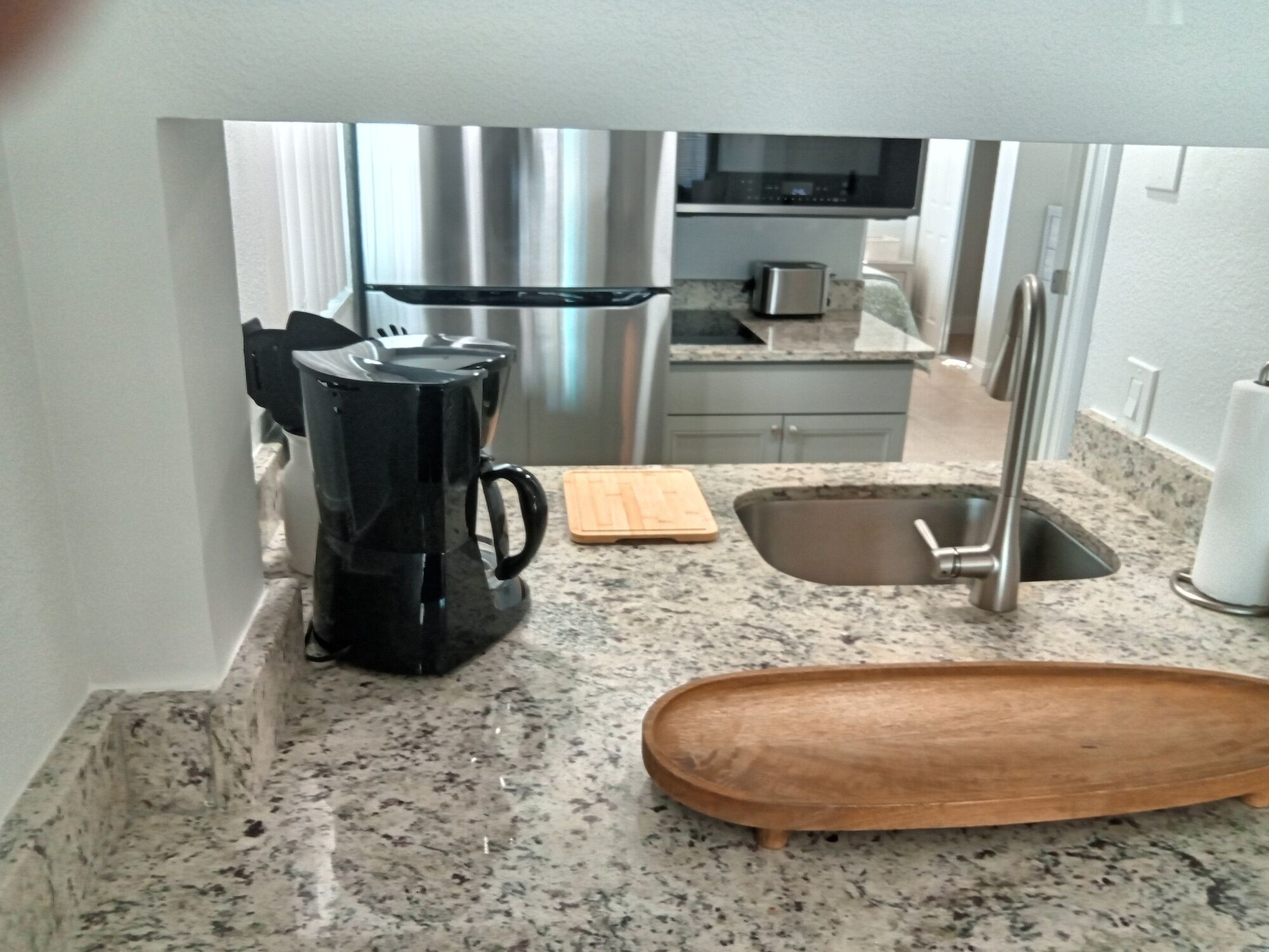 A kitchen with a coffee maker, a cutting board, a sink, and a wooden tray.