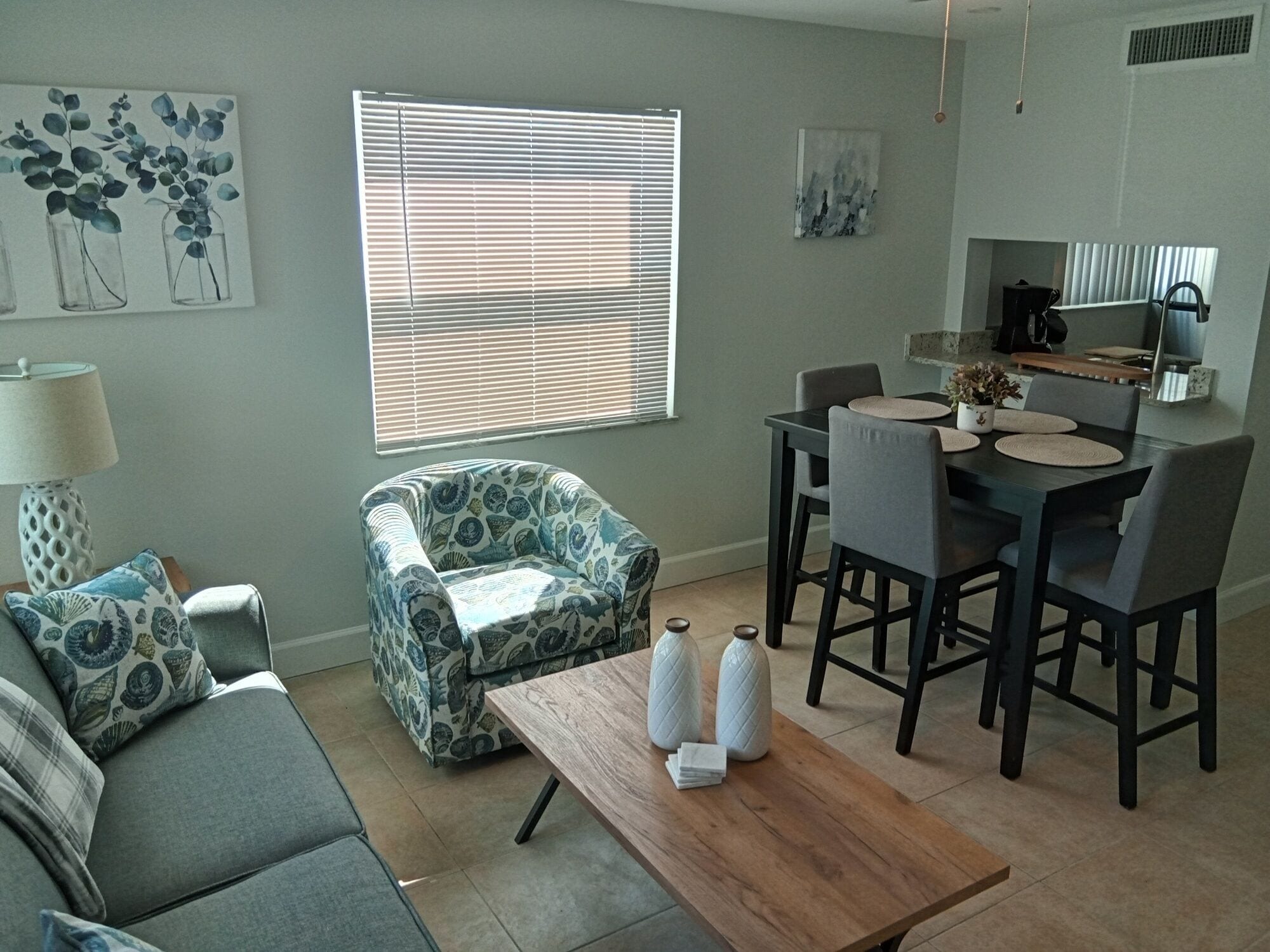A living room with a sofa, a patterned armchair, a wooden coffee table, and a dining area with a table and chairs.