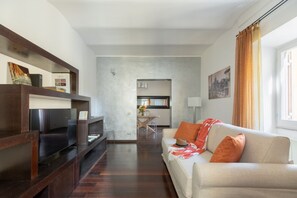 Ein modernes Wohnzimmer mit einer Couch, einem Couchtisch und einem Bücherregal. Im Hintergrund ist ein Essbereich mit Tisch und Stühlen zu sehen.