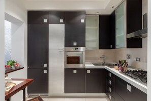 A modern kitchen with dark cabinetry, a stainless steel range hood, and a built-in oven. - iFlat | Elegant Roman Retreat by the Vatican (Roma)