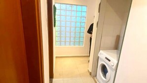 Een wasserette met een wasmachine, een raam met uitzicht en een betegelde vloer.