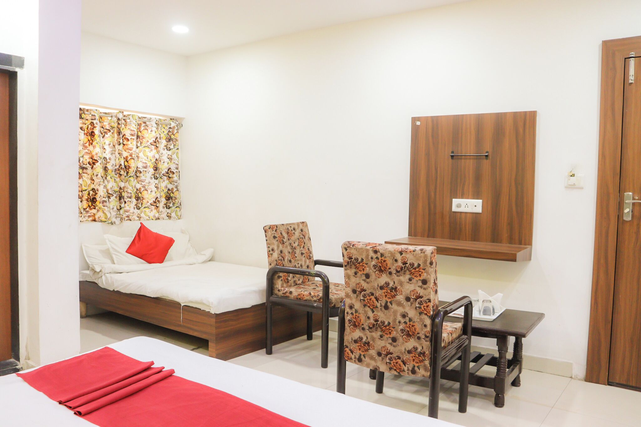 A hotel room with a bed, two chairs, a small table, a wooden cabinet, and a curtain with a floral pattern.