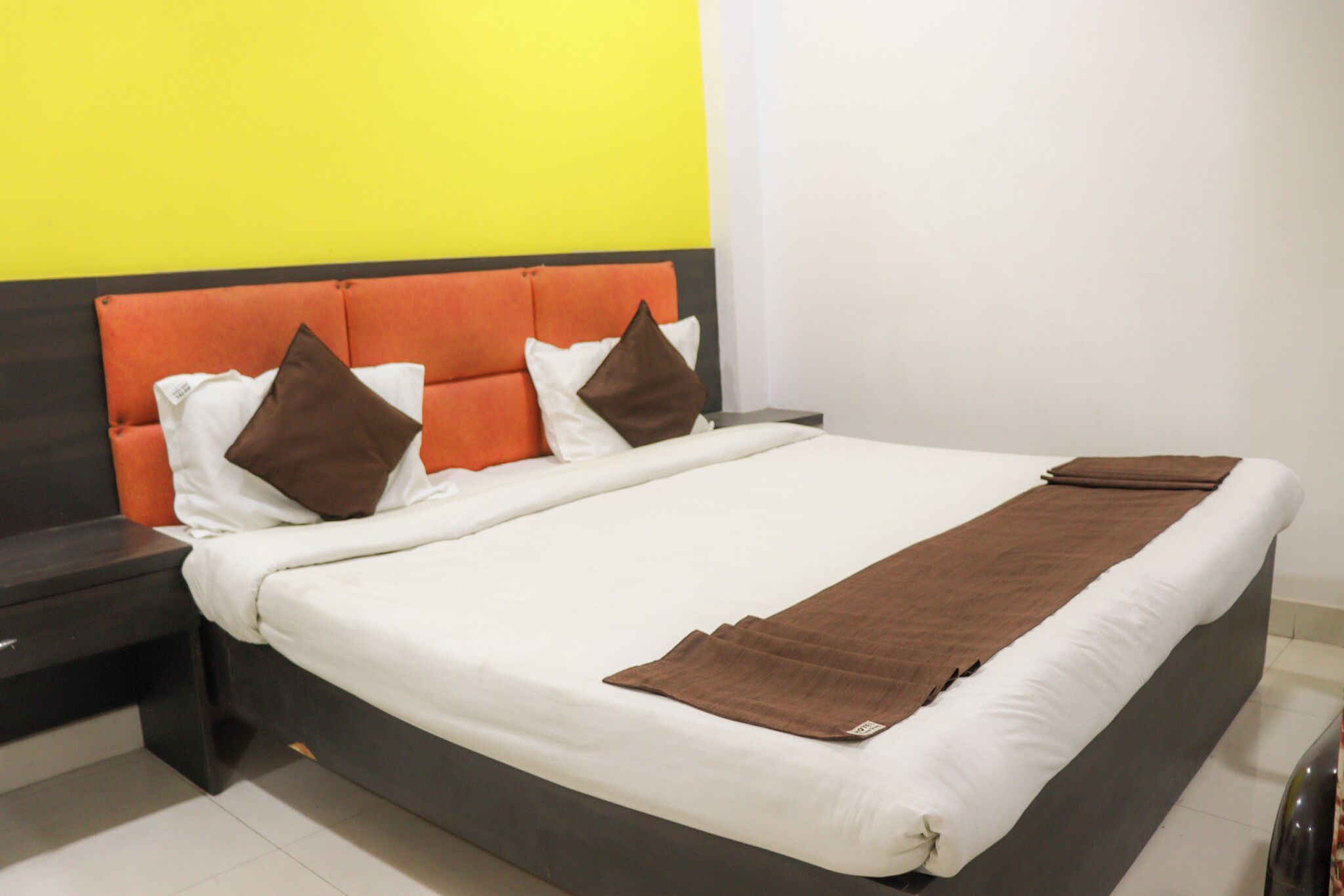 Ein Hotelzimmer mit Bett, Nachttischen und einer leuchtend gelben Wand.