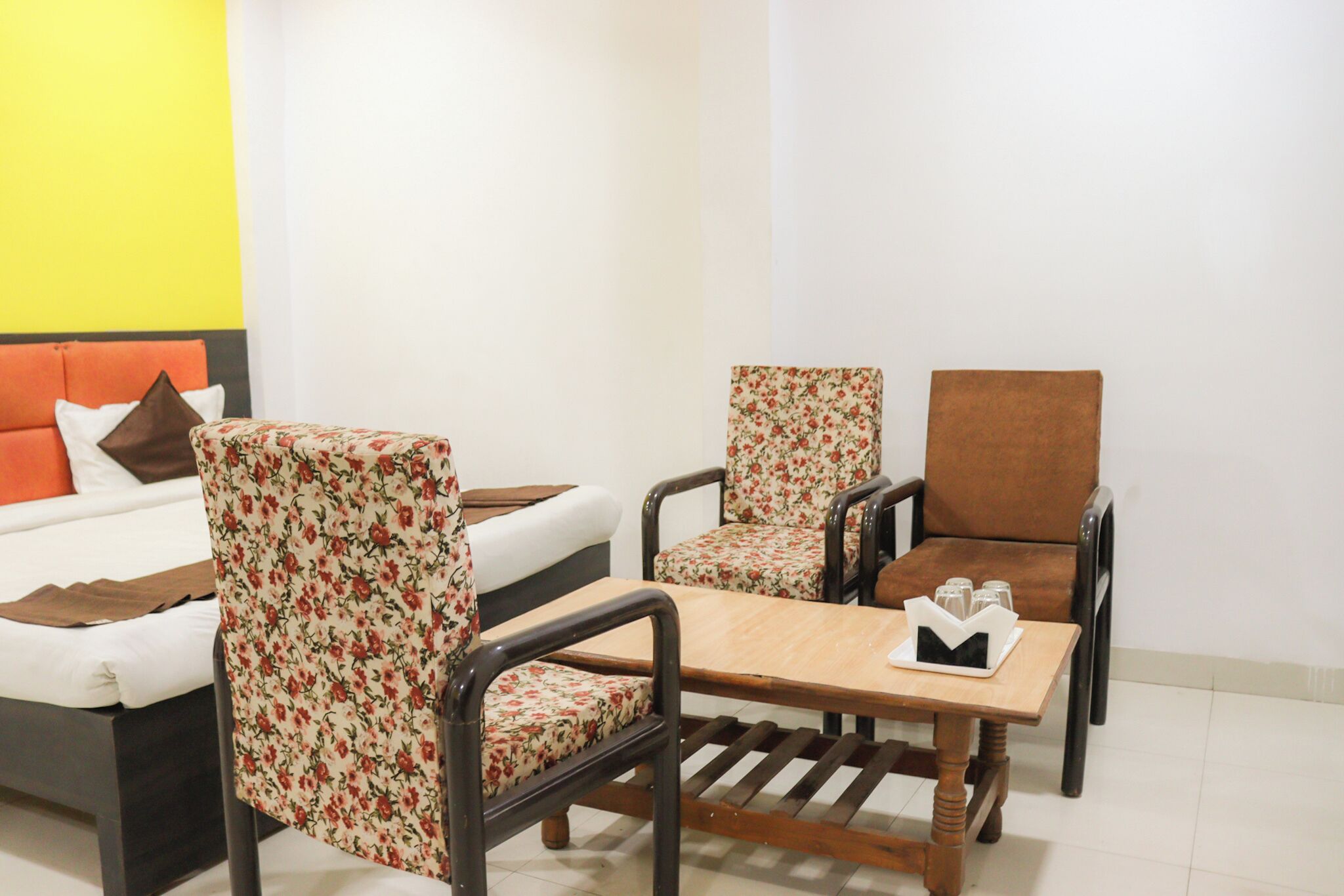 Une pièce comprenant un lit, deux fauteuils à motifs floraux, une table en bois et un fauteuil marron.