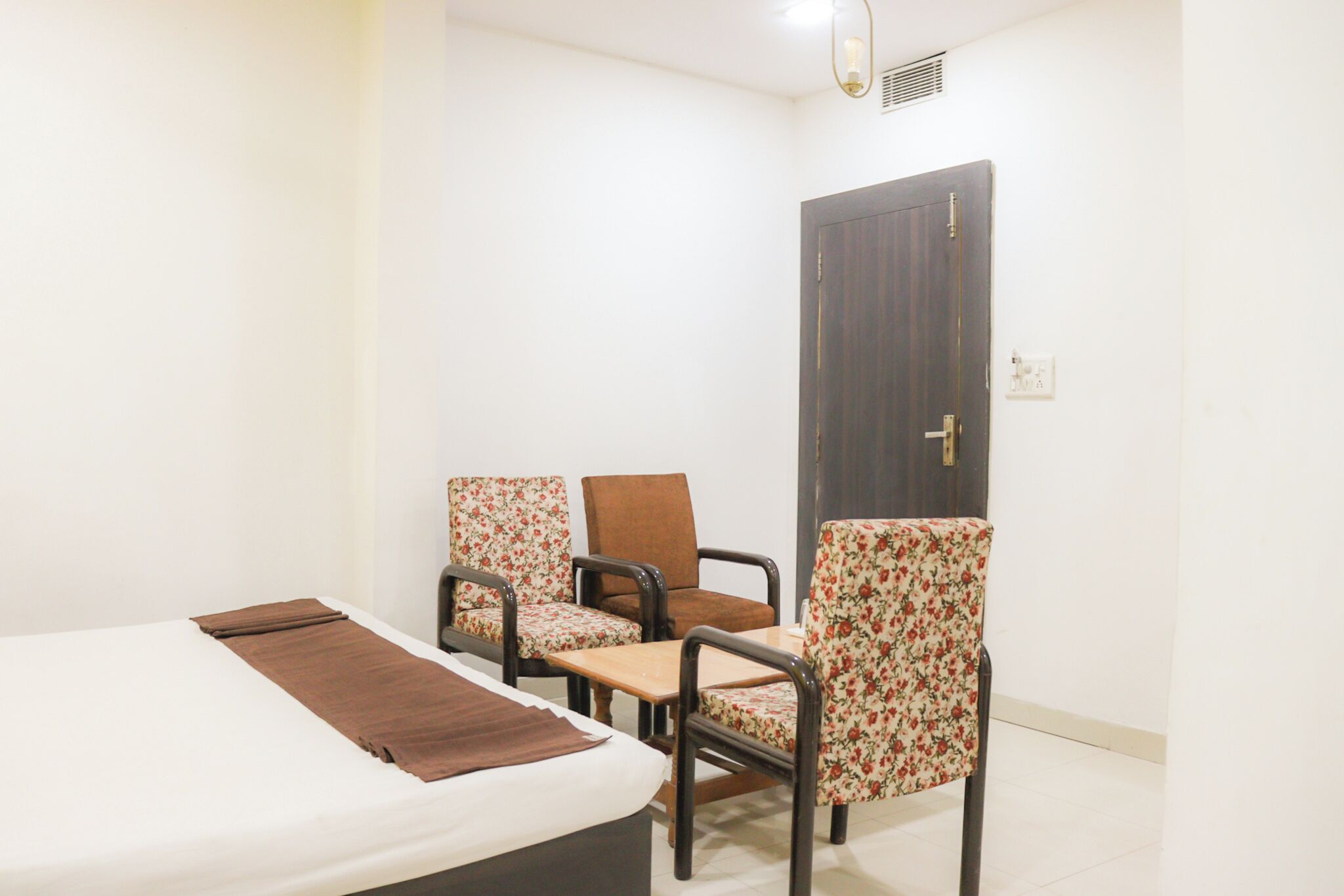 Una habitación de hotel con una cama, dos sillas, una mesita y una puerta.