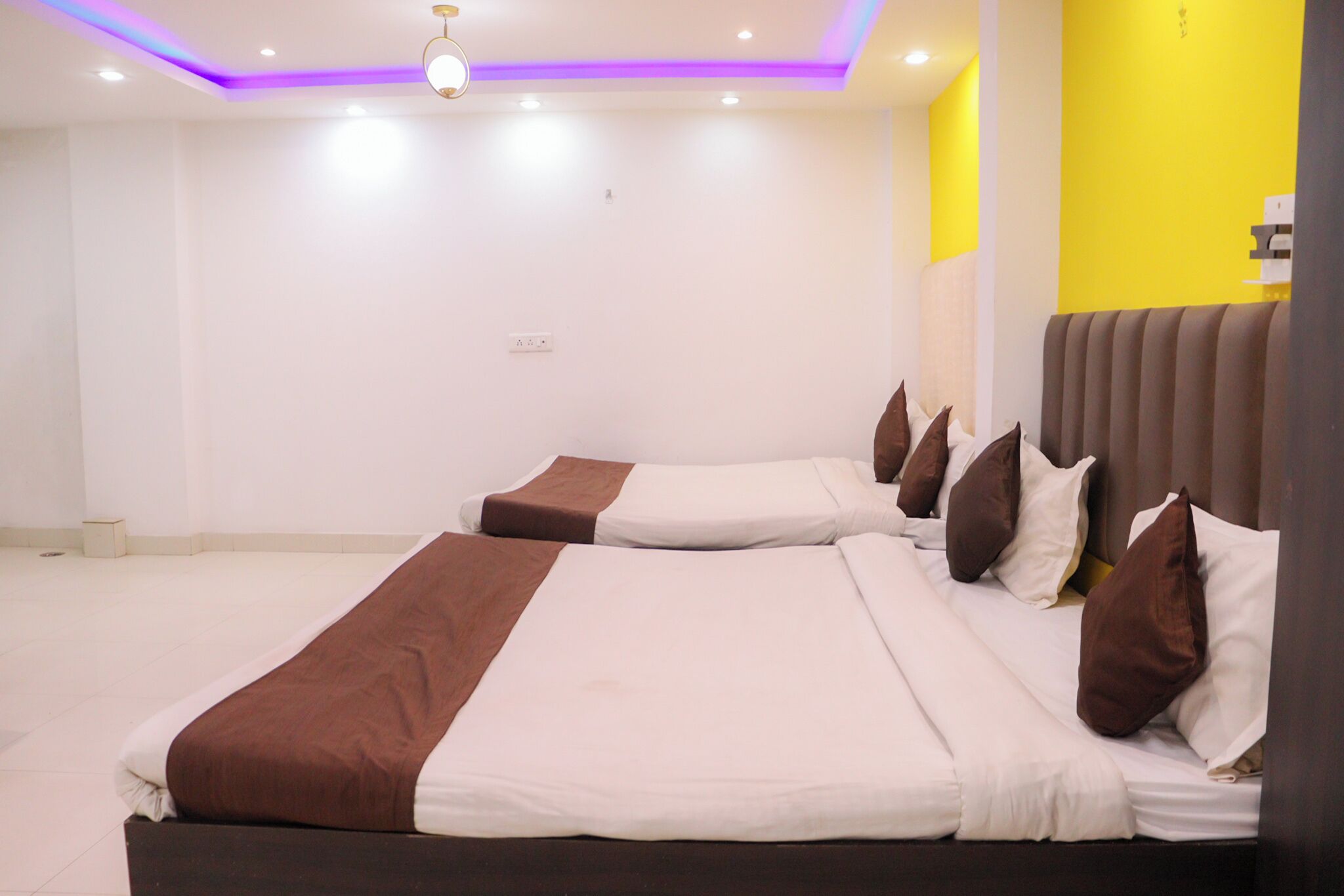 Quarto de hotel com duas camas, uma luminária no teto e uma parede com detalhes em amarelo.