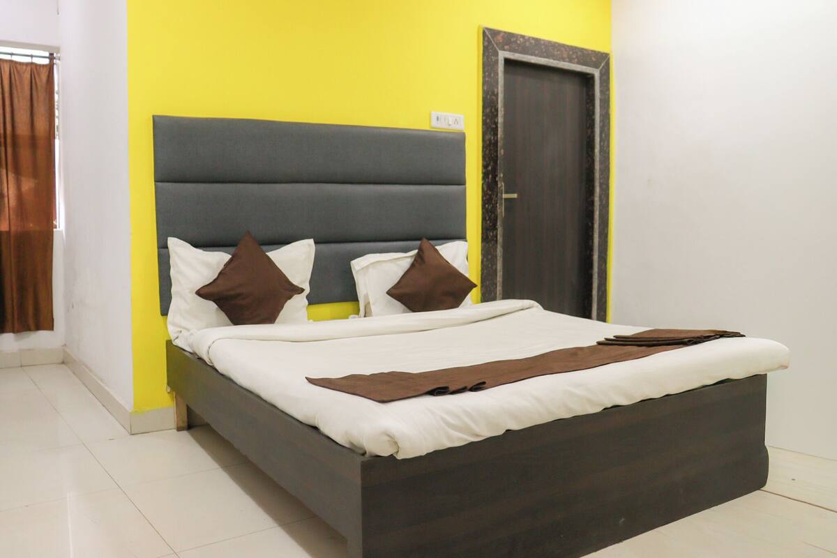 A bed with a dark headboard, white bedding, and brown pillows in a room with yellow walls and a wooden door.