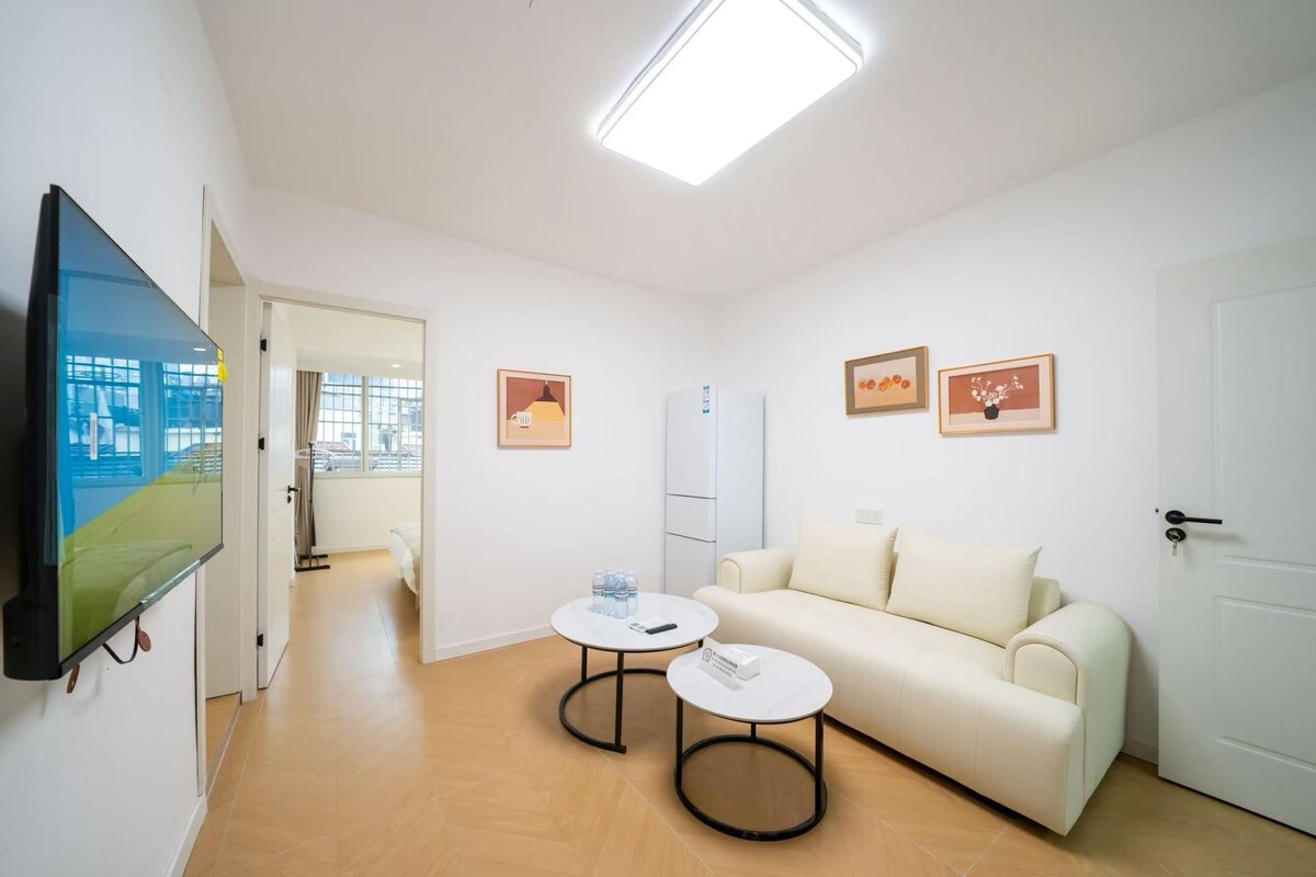 Un salon moderne avec un téléviseur à écran plat, un canapé blanc, deux tables rondes et une porte.