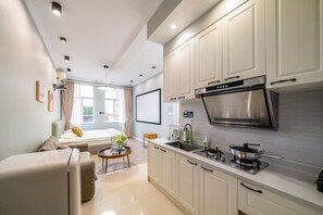 A modern kitchen with white cabinets, a stainless steel range hood, and a dining area with a sofa and coffee table.