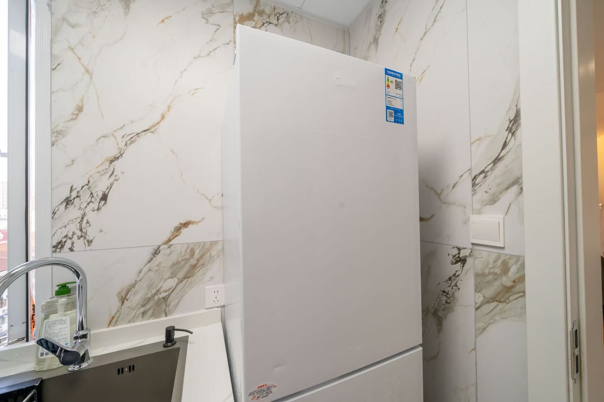 Une cuisine avec un réfrigérateur blanc, un évier avec un robinet et des murs à motifs de marbre.