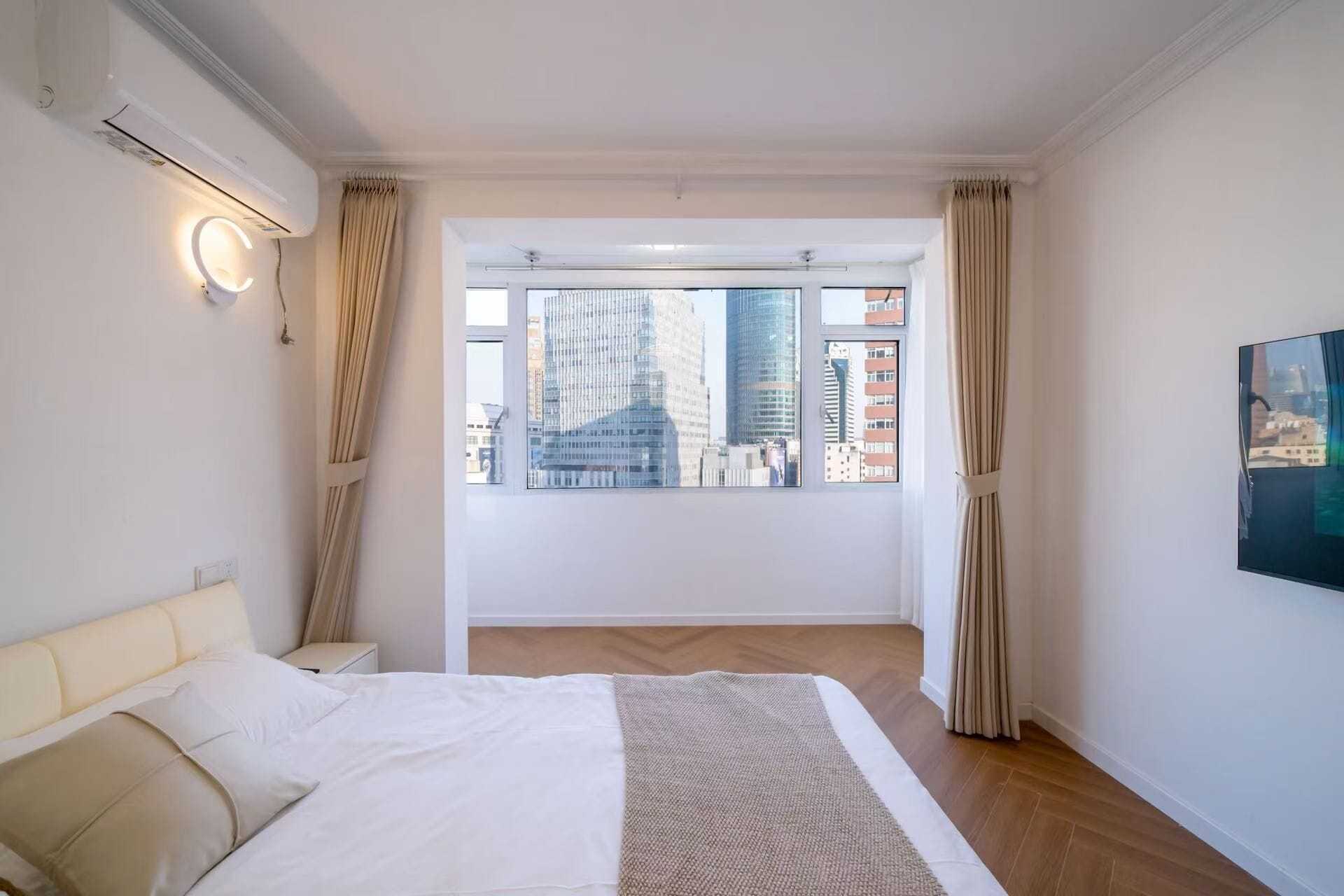 Ein Schlafzimmer mit Bett, einem Fenster mit Vorhängen, einer Wandleuchte und einem Gemälde.