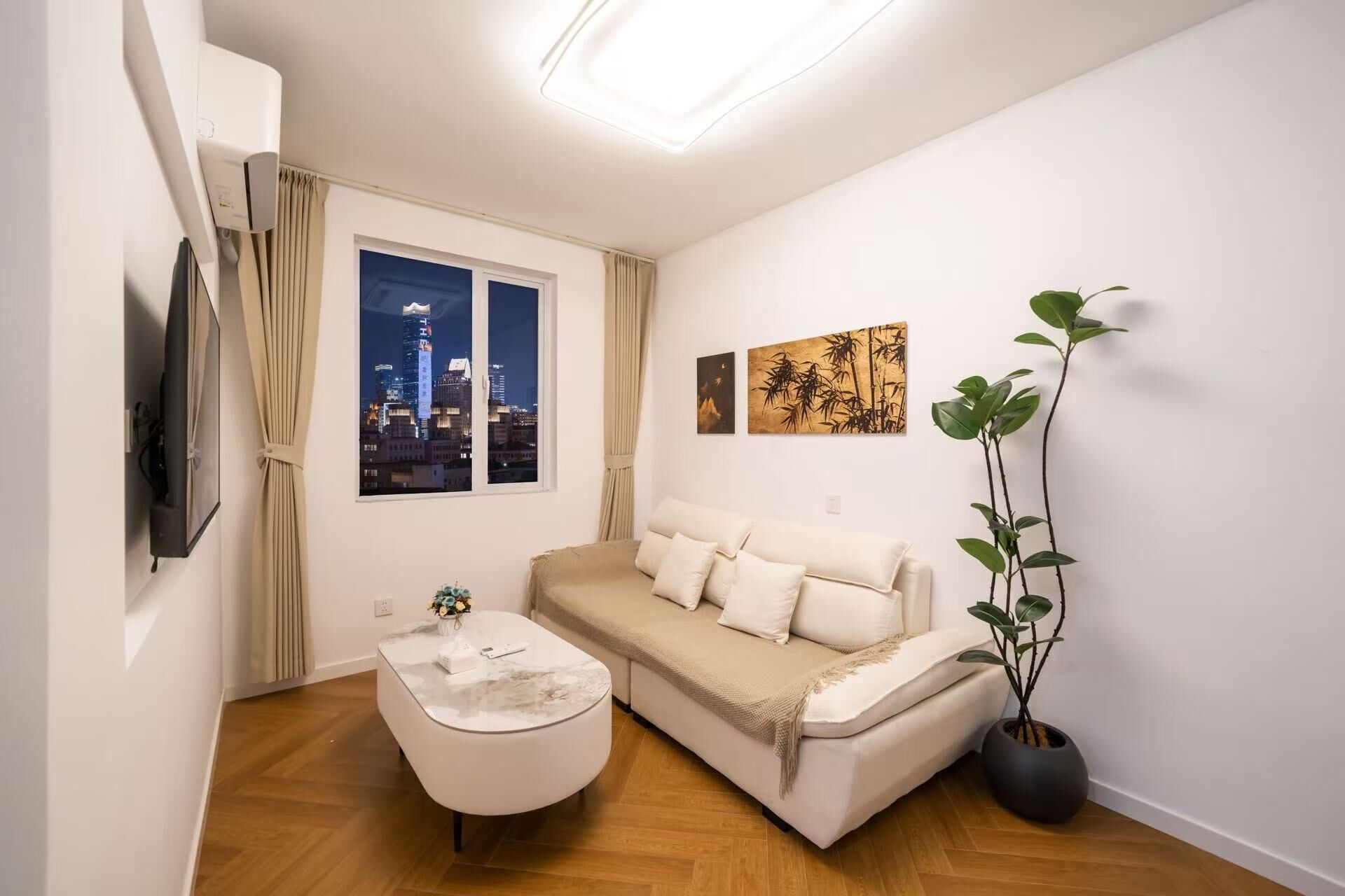 A modern living room with a sofa, a coffee table, a potted plant, and a cityscape view through the window.