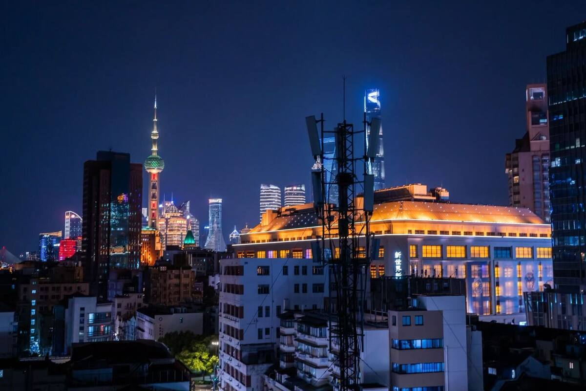 Une vue nocturne d’une ville, avec des bâtiments illuminés, dont une tour imposante surmontée d’une sphère.
