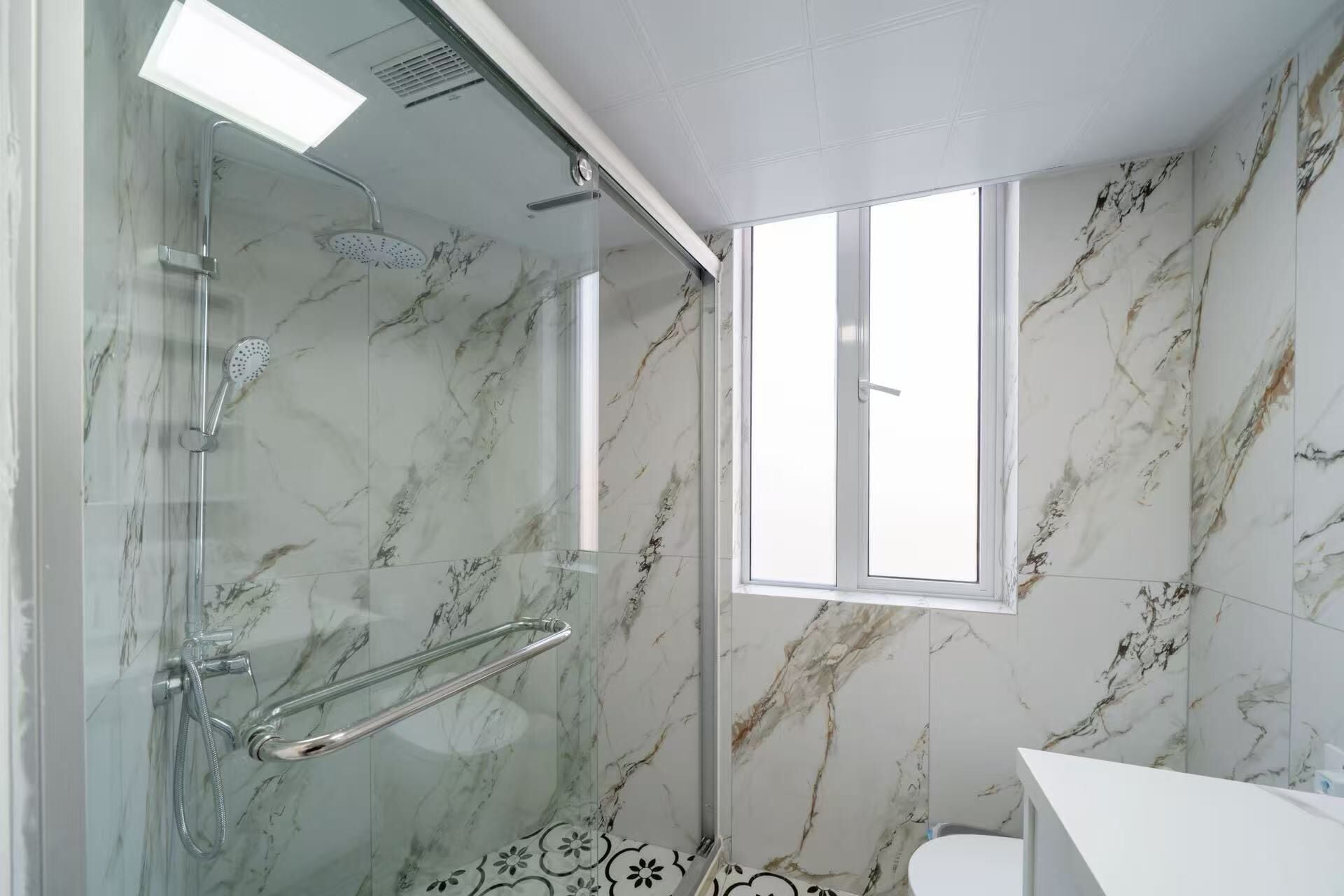 A bathroom with a glass-enclosed shower, a toilet, and a window.
