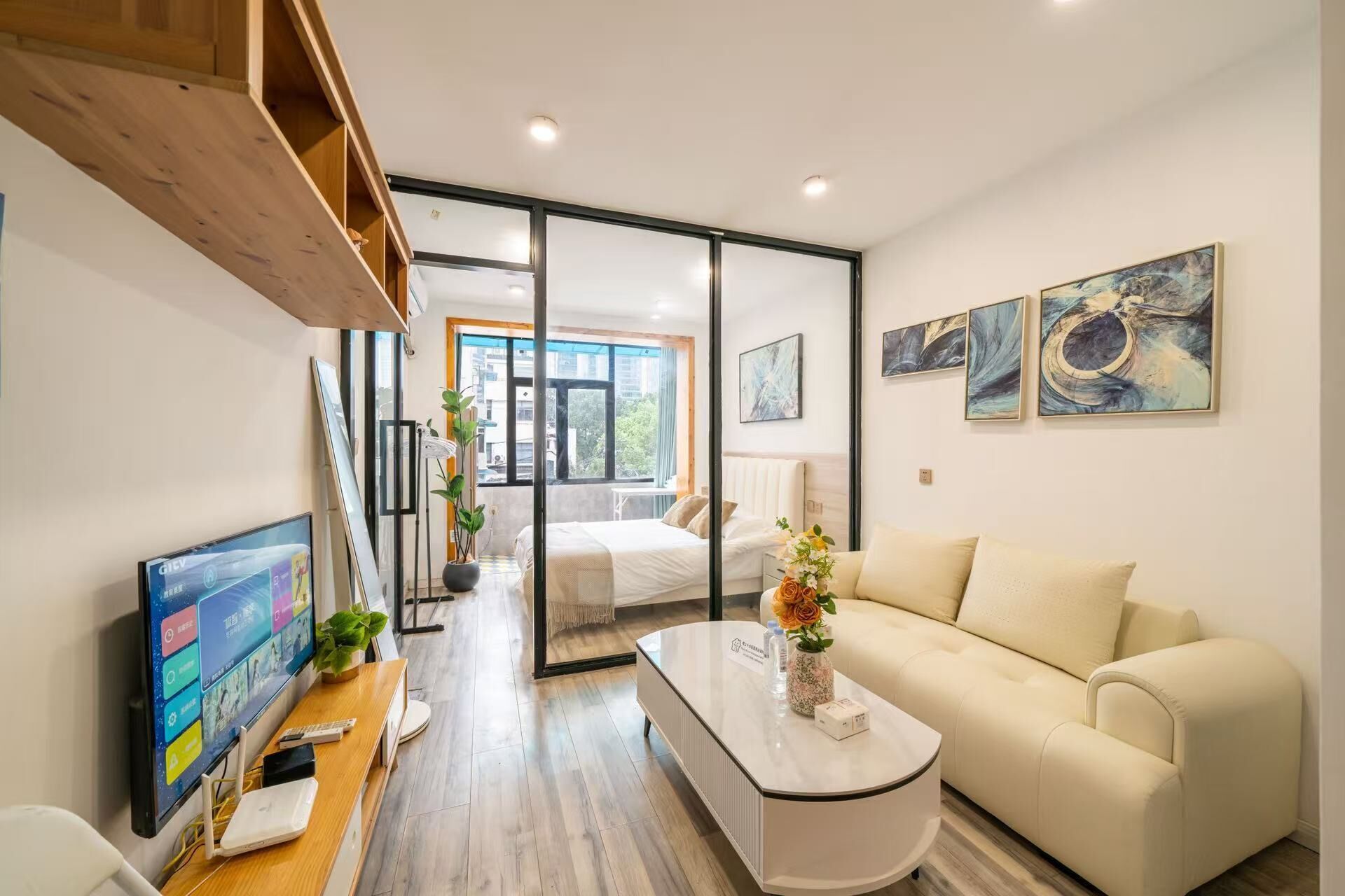 Una habitación de hotel moderna con cama, sofá, escritorio con computadora y televisión. Hay cuadros en la pared y una ventana con vistas a edificios.