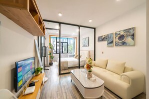 Een moderne hotelkamer met een bed, een bank, een bureau met een computer en een televisie. Er hangen schilderijen aan de muur en een raam met uitzicht op gebouwen.