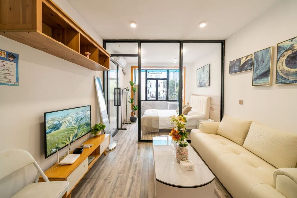 Een moderne woonkamer met een flatscreen televisie, een bank, een salontafel en een schuifpui naar een balkon.