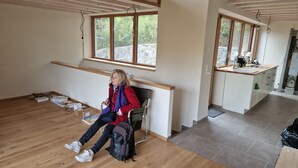 A room with a wooden floor, a bench, a chair, a suitcase, and a kitchen area with a countertop and sink. - Self-sufficient eco-house: water, electricity, internet (Solopisky)