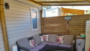 Ein überdachter Patio-Bereich mit einer Eckcouch, einem kleinen Tisch und einem Kühlschrank.
