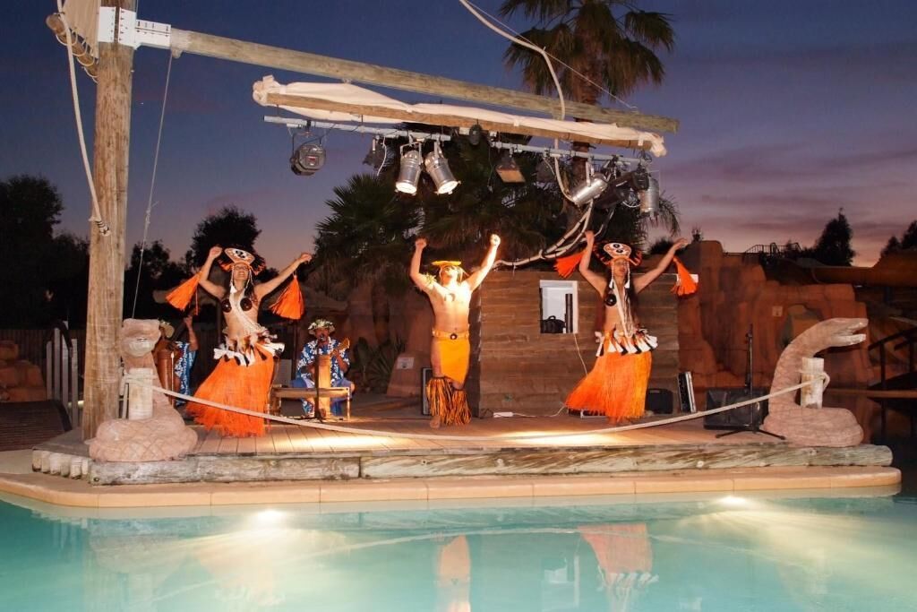 Un escenario con artistas disfrazados, una estructura de madera sobre él y una piscina al frente.