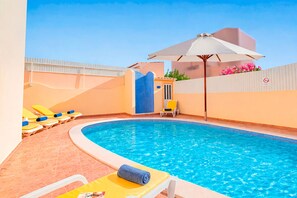 A swimming pool with lounge chairs and an umbrella.