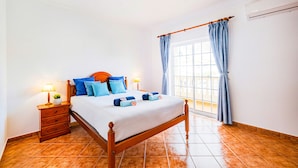 A bedroom with a wooden bed, a nightstand with a lamp, a window with curtains, and a tiled floor. - Villa with Pool and BBQ in Galé, Albufeira (Albufeira)
