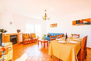 Un salon spacieux avec une cheminée, un canapé, une table à manger pour quatre personnes et une grande fenêtre.
