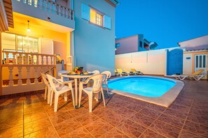 Un espace aménagé au bord de la piscine, comprenant une table et des chaises, une piscine et un balcon doté d’une balustrade.