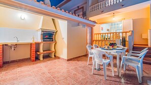 An outdoor patio with a grill, dining table, chairs, and a view of the building's interior. - Villa with Pool and BBQ in Galé, Albufeira (Albufeira)