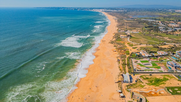 An aerial view of a coastal area with a sandy beach, a clear blue ocean, and a mix of residential and commercial buildings. - Villa with Pool and BBQ in Galé, Albufeira (Albufeira)