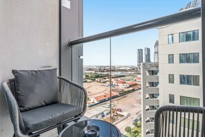 A balcony with a wicker chair and a small table, overlooking a cityscape with buildings and a construction site. - Stayshort - Beautiful 1 Bed Apartment in Business Bay That Sleeps 4 (Dubai)