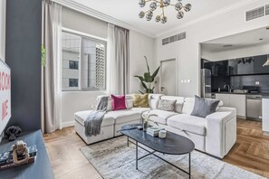 A modern living room with a white sofa, a black coffee table, and a view of the city through large windows. - Stayshort - Beautiful 1 Bed Apartment in Business Bay That Sleeps 4 (Dubai)