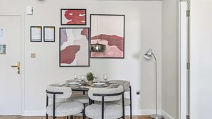 Un comedor con una mesa redonda, cuatro sillas tapizadas en gris y cuadros en la pared.
