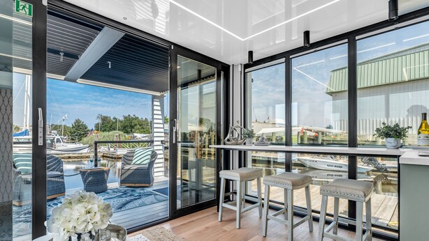 A modern interior with a glass door leading to a balcony with outdoor seating and a view of boats.